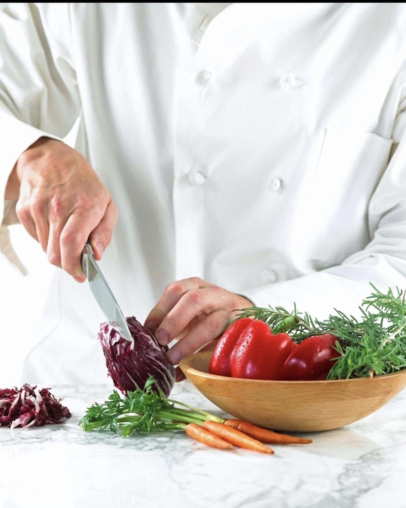 A chef slicing radicchio beside a wooden bowl of peppers, rosemary and carrots