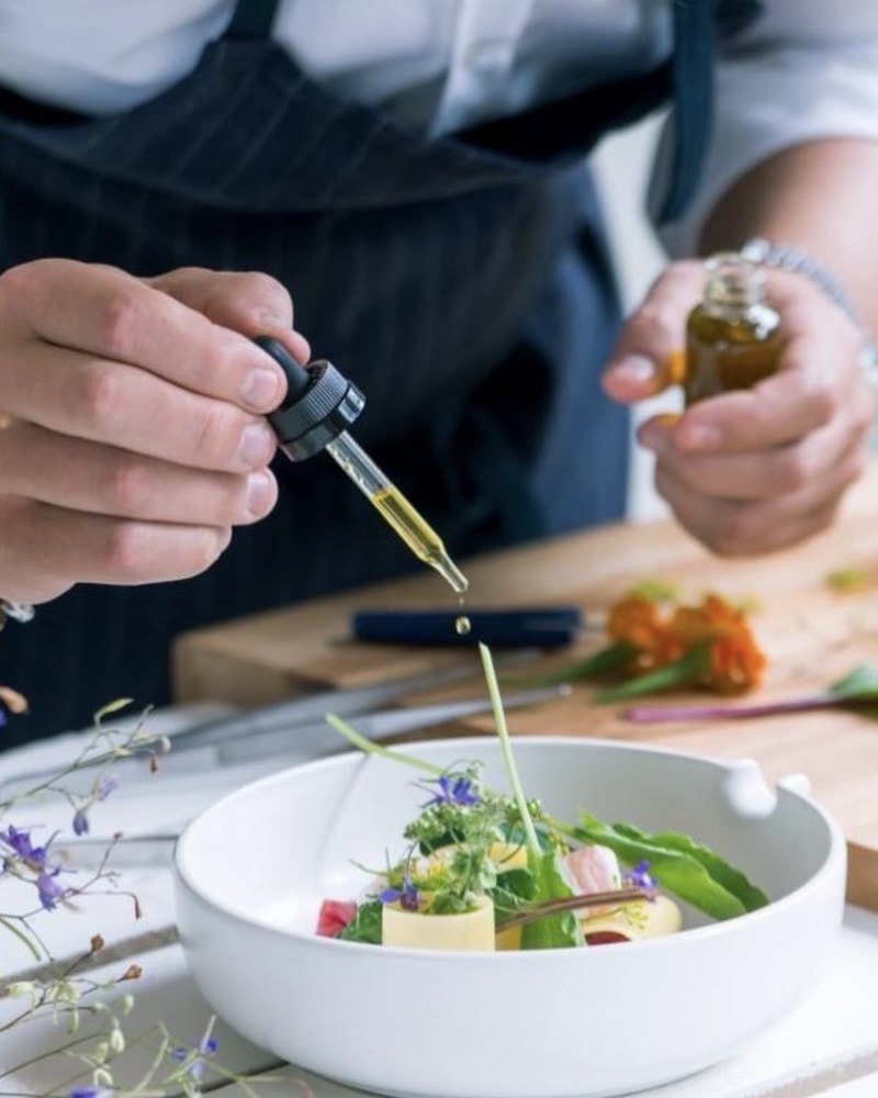 A chef finishing a plated dish with olive oil from a dropper